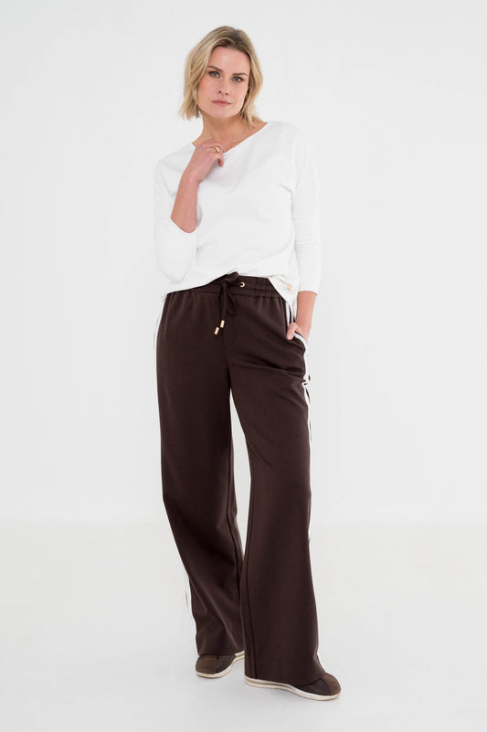 dame draagt een leuke outfit met bruine broek met witte strepen aan de zijkant gecombineerd met een wit shirt