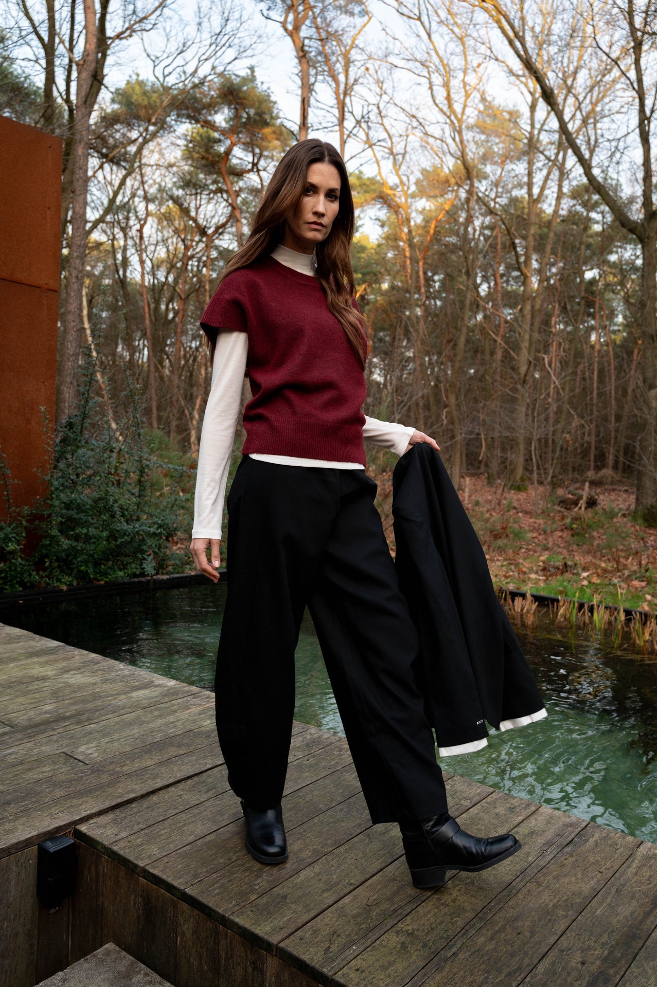 model draagt de zwarte barrel broek vadou met een rood t-shirt over een witte coltrui en heeft een zwarte blazer in haar hand