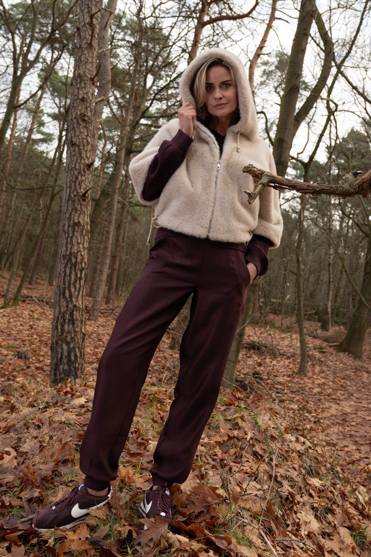 dame draagt in het bos de voss broek wijnrood met steekzakken gecombineerd met een blouse in dezelfde kleur en daarover een warm zacht jasje met korte mouwen