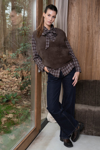 dames najaarslook met donkere spijkerbroek, bruine mouwloze top en geruite strikblouse