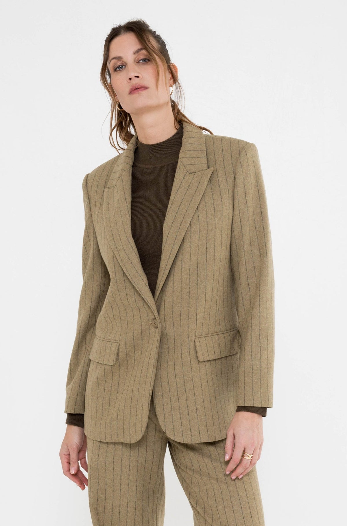 model draagt de blazer rora khaki gestreept bovenop de broek en met mosgroene coltrui