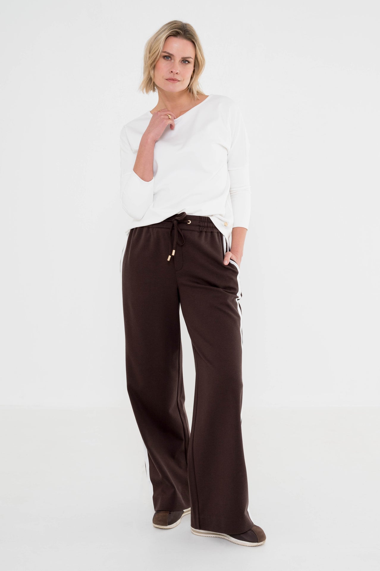 dame draagt een leuke outfit met bruine broek met witte strepen aan de zijkant gecombineerd met een wit shirt