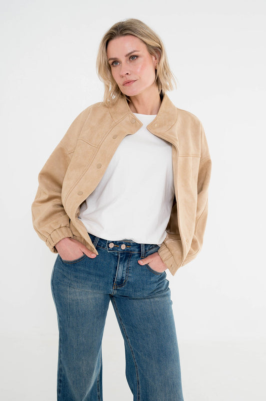 model draagt een suedelook jasje in camekleur op een spijkerbroek gecombineerd met een wit shirt eronder