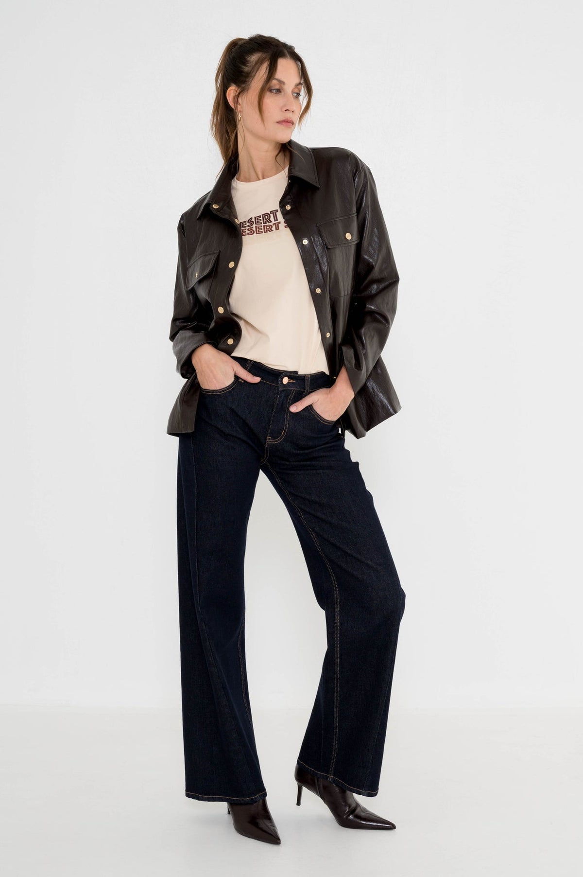 model draagt donkerblauwe denim met een bruine leatherlook jasje en een t-shirt eronder